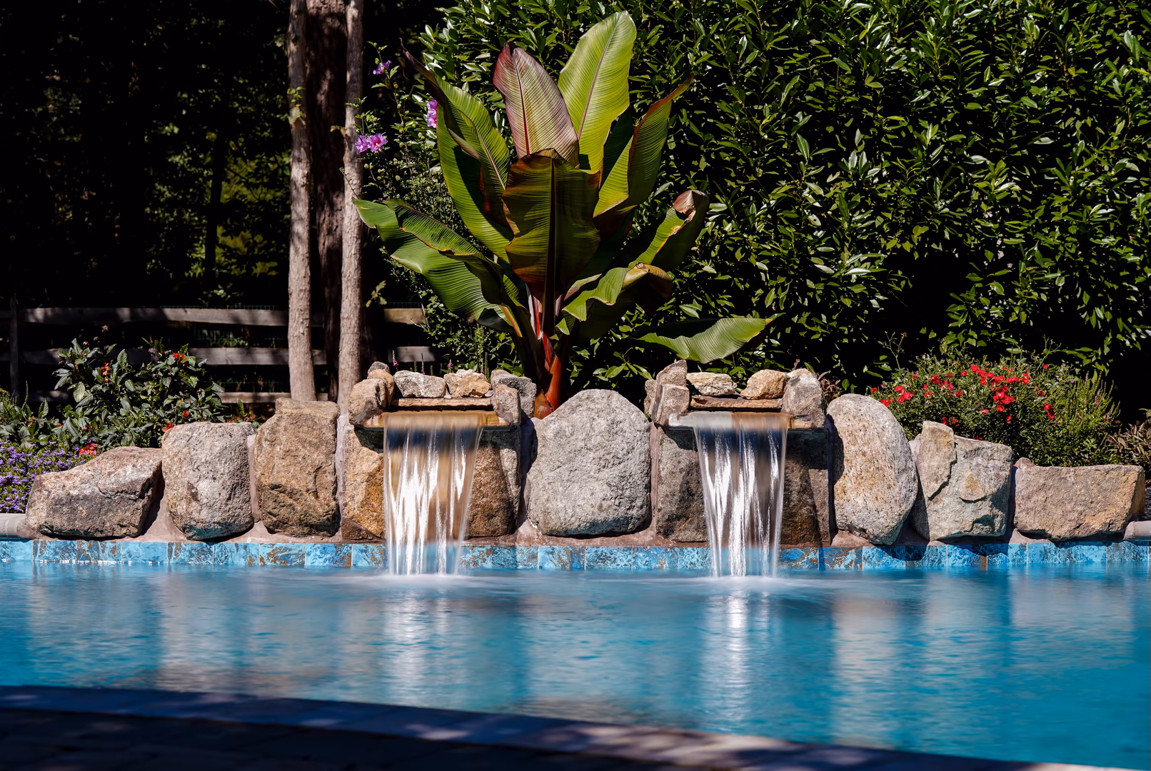 Twin natural stone boulder waterfalls cascading into a pool with lush tropical landscaping