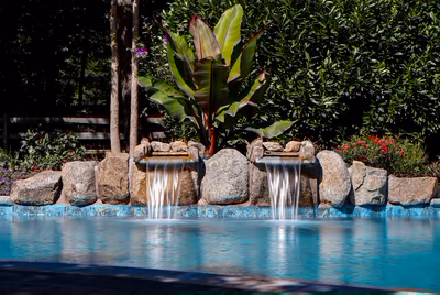 Twin single-tier natural stone boulder waterfalls cascading into a pool with lush tropical landscaping