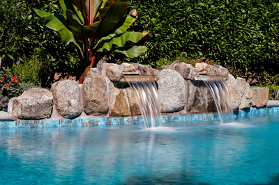Twin natural stone boulder waterfalls cascading into a tiled pool with lush tropical landscaping