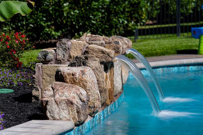 Natural stone boulder waterfalls cascading twin streams into a pool with lush garden landscaping