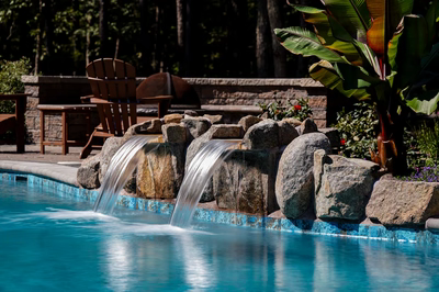 Twin natural stone boulder waterfalls cascading into a pool surrounded by lush tropical plants