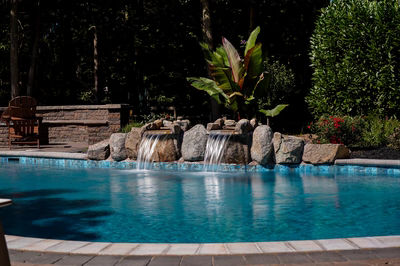 Dual natural stone boulder waterfalls cascading into a blue pool with lush tropical landscaping