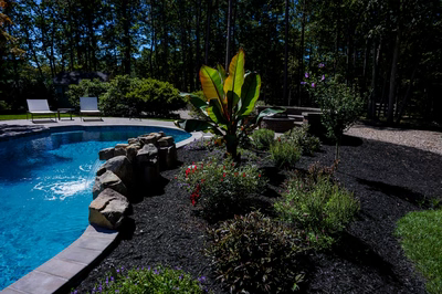 Multi-tiered natural stone boulder waterfall cascading into a freeform pool surrounded by tropical landscaping