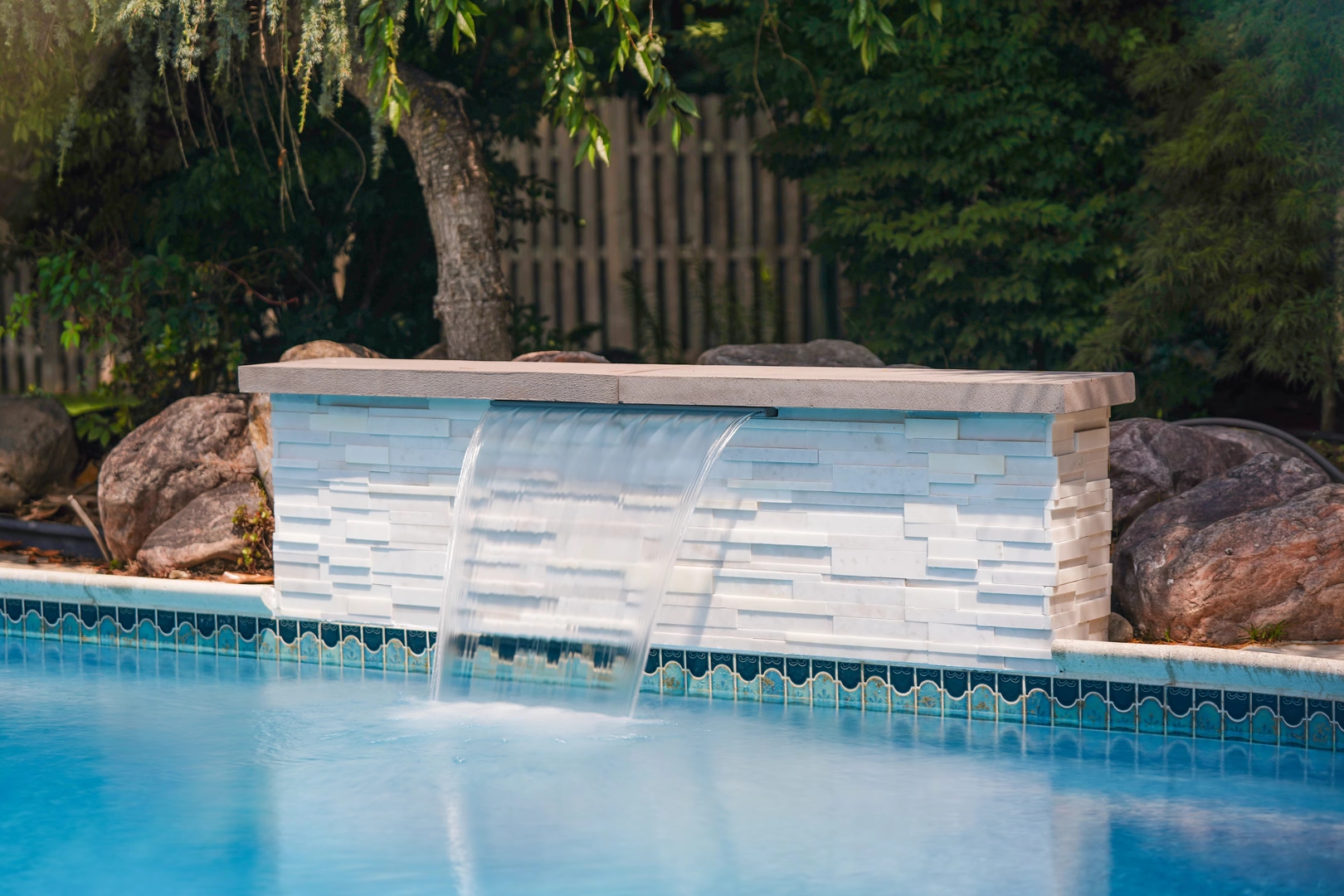 Natural stone boulder waterfall cascading into a pool surrounded by lush garden plants