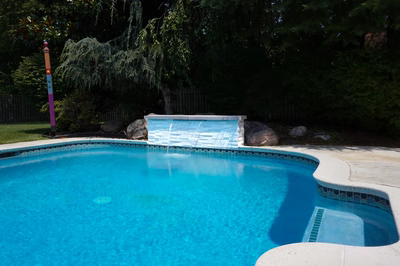 Single-tier natural stone boulder waterfall cascading into a pool surrounded by lush garden plants