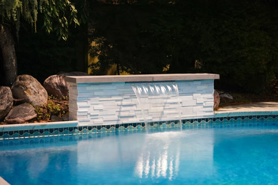 Single-tier sheet waterfall cascading from white stone wall into pool with surrounding boulders and plants