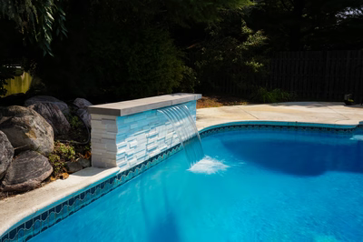Single-tier sheer descent waterfall spilling into a pool bordered by boulders and dense foliage