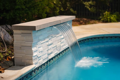 Single-tier sheet waterfall flowing from stacked stone into a pool surrounded by lush greenery