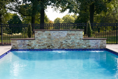 Three-tiered natural stone boulder waterfall cascading into a pool with surrounding trees and shrubs