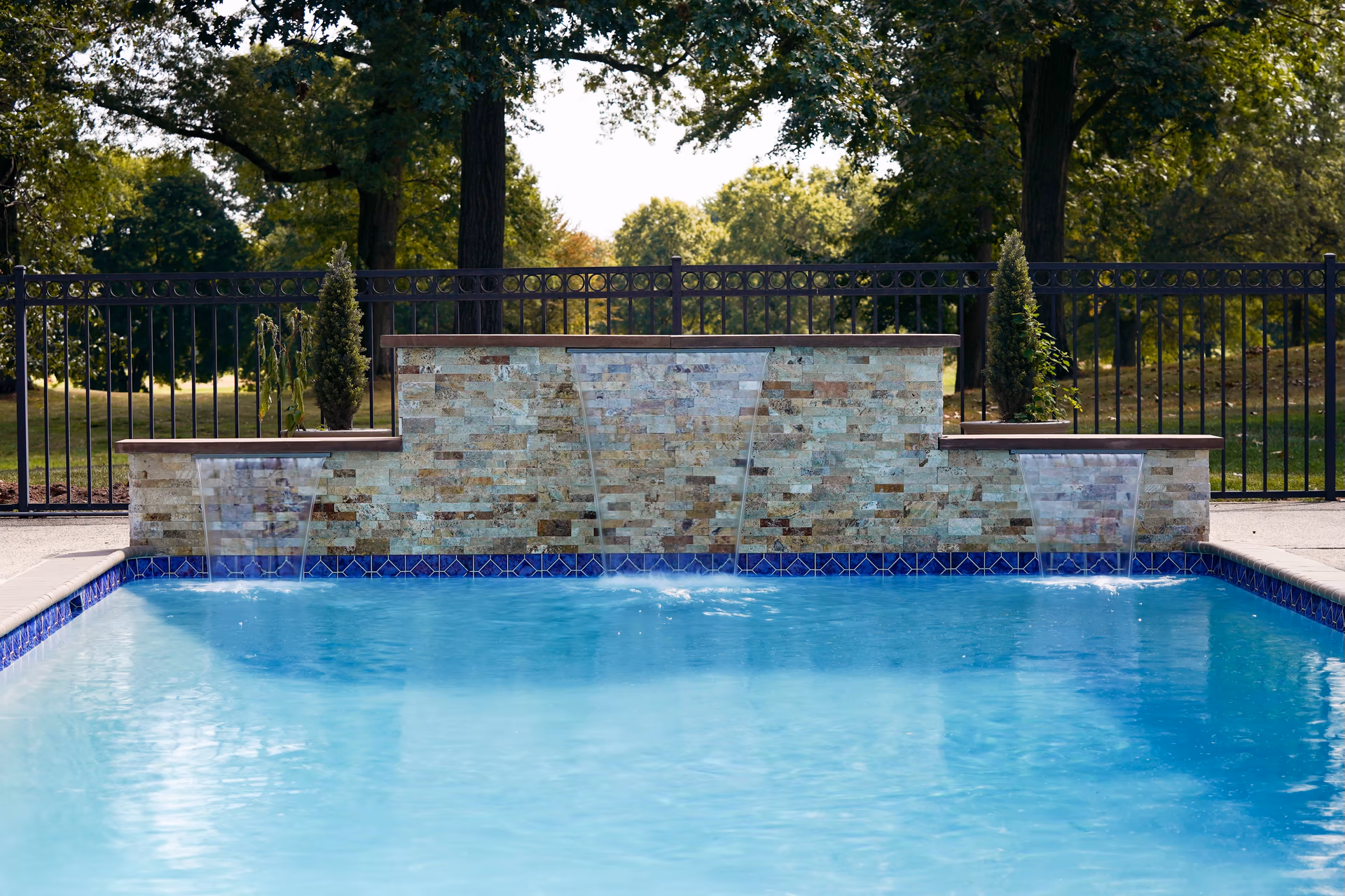 Three-tiered natural stone boulder waterfall cascading into a pool with surrounding trees and shrubs