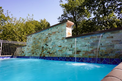 Two-tiered sheer descent stone waterfalls flowing into a swimming pool bordered by green trees