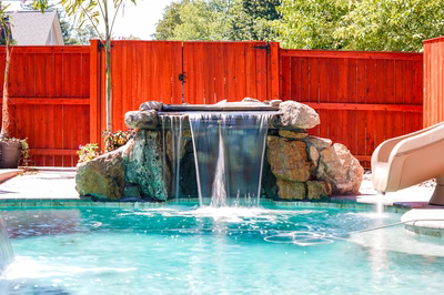 Single-tier natural stone boulder waterfall with sheet-like flow cascading into a pool near plants