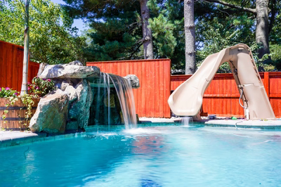 Multi-tiered natural stone boulder waterfall cascading into a pool with surrounding trees and plants