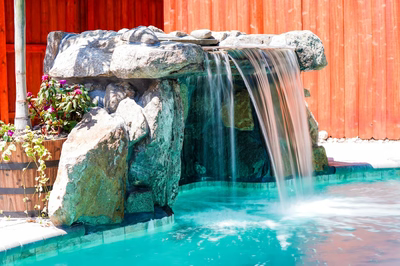 Single-tier natural stone boulder waterfall cascading into a pool with vibrant potted flowering plants