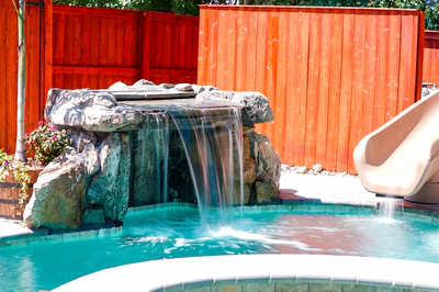 Single-tier natural stone boulder waterfall cascading into a pool with vibrant garden plants