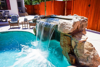 Single-tier natural stone boulder waterfall cascading into a pool beside a wooden fence