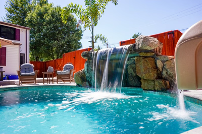 Single-tier natural stone boulder waterfall cascading into a pool beside a tropical palm tree