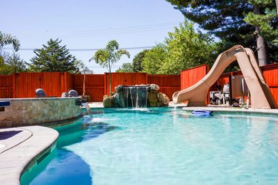 Multi-tiered natural stone boulder waterfall cascading into a freeform pool with tropical landscaping