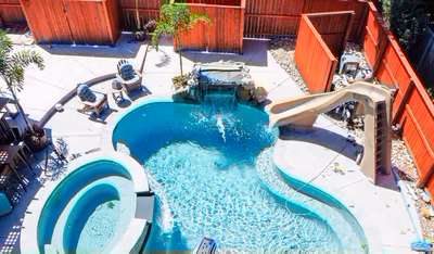 Two-tiered natural stone boulder waterfall cascading into a freeform pool with tropical landscaping