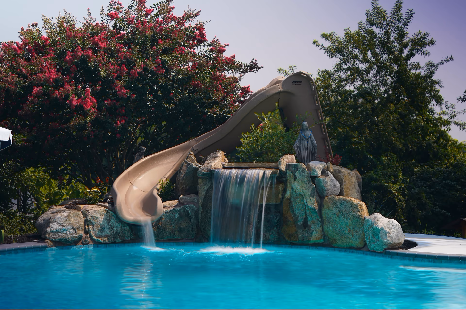 Single-tier natural stone boulder waterfall cascading into a pool framed by lush pink blossoms