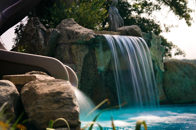 Two-tiered natural stone boulder waterfall cascading into a pool with lush surrounding garden greenery
