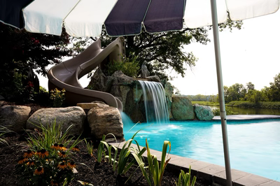 Single-tier natural stone boulder waterfall cascading into pool with slide and garden plants