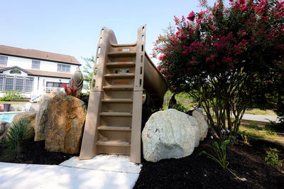 Multi-tiered natural stone boulder waterfall cascading into a backyard pool near vibrant flowering trees