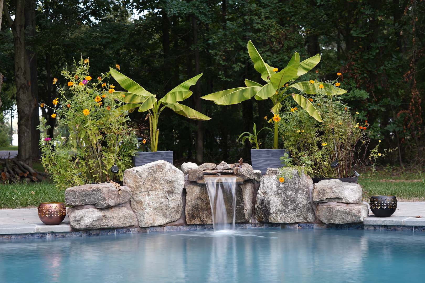Natural stone boulder waterfall cascading into a pool surrounded by lush tropical plants