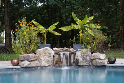Single-tiered natural stone boulder waterfall cascading into a pool surrounded by lush tropical plants
