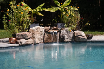 Single-tier natural stone boulder waterfall cascading into pool surrounded by lush tropical plants and flowers