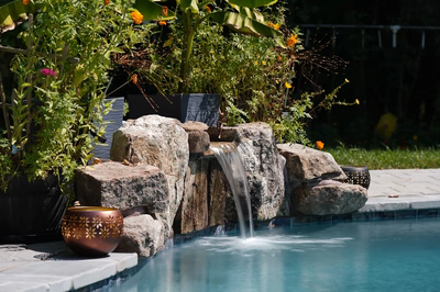 Single-tier natural stone boulder waterfall cascading into pool water surrounded by lush garden plants