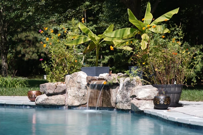 Single-tier natural stone boulder waterfall cascading into a pool surrounded by lush tropical plants