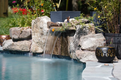 Single-tier natural stone boulder waterfall cascading into a pool surrounded by lush garden plants