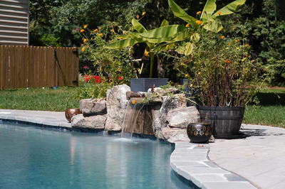 Single-tier natural stone boulder waterfall cascading into a pool with lush tropical plants