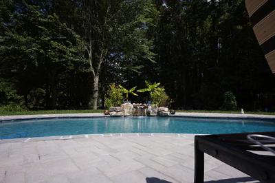 Single-tiered natural stone boulder waterfall cascading into a pool with lush tropical plants nearby