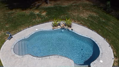 Two-tiered natural stone boulder waterfall cascading into a freeform pool with surrounding tropical plants