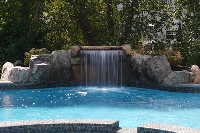 Single-tier natural stone boulder waterfall cascading into a blue pool with lush green foliage