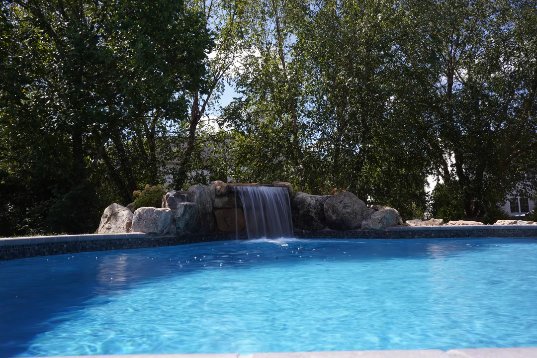 Single-tier natural stone boulder waterfall with sheet flow cascading into a pool among lush trees