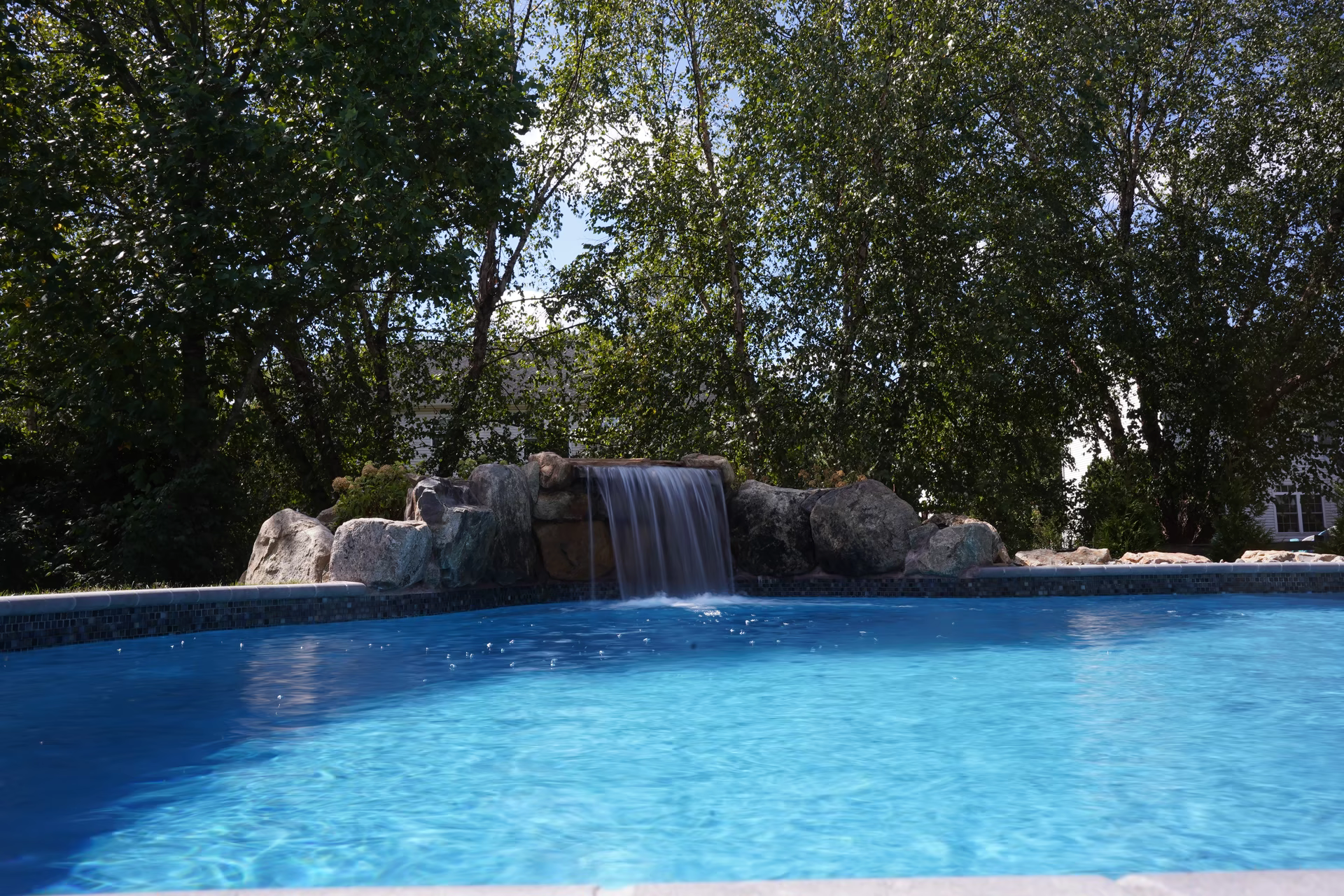 Single-tier natural stone boulder waterfall with sheet flow cascading into a pool among lush trees