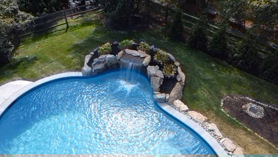 Single-tier natural stone boulder waterfall cascading into a clear pool with lush garden plantings