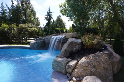 Single-tier natural stone boulder waterfall cascading into a pool surrounded by lush garden greenery