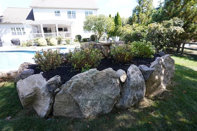 Natural stone boulder waterfall cascading into a swimming pool surrounded by lush garden plants