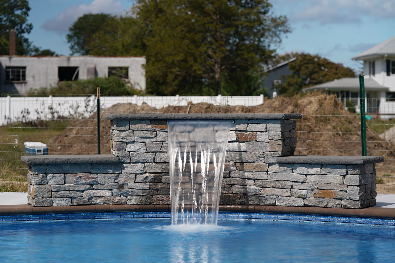 Natural stone waterfall with sheer descent flow cascading into a backyard swimming pool