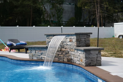 Three-tiered natural stone waterfall pours a sheer sheet into a pool with backyard trees