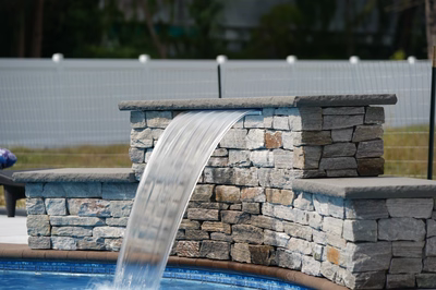 Multi-tiered natural stone waterfall cascading a sheer sheet of water into a pool