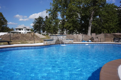 Multi-tiered natural stone boulder waterfall cascading into a blue swimming pool with surrounding greenery
