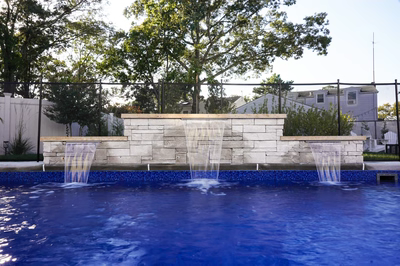 Three-tiered natural stone boulder waterfalls cascading into a blue pool with lush backyard trees