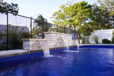 Three-tiered natural stone boulder waterfall cascading into a pool surrounded by lush green trees