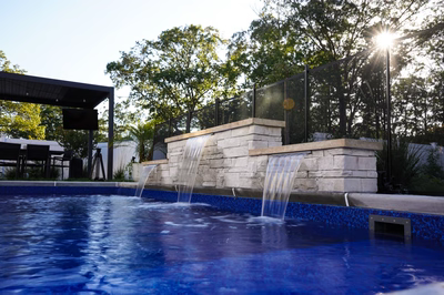 Three-tiered stacked stone sheer waterfalls cascading into a blue pool with surrounding garden greenery