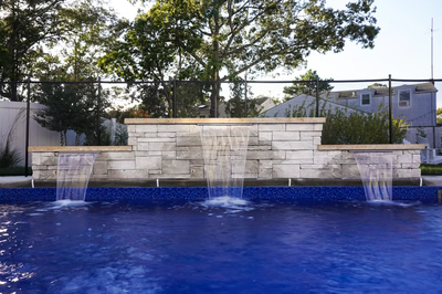 Three-tiered natural stone sheer descent waterfalls cascading into a blue pool with backyard trees
